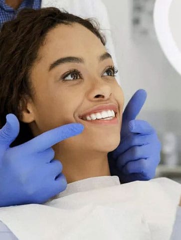 Woman smiling during dental examination with gloved dentist hands in clinical setting.