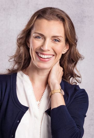 Professional woman smiling at camera in dental office portrait wearing navy cardigan and white blouse.