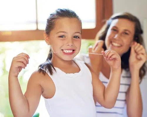 Young child and adult brushing teeth together in bright bathroom, smiling happily.