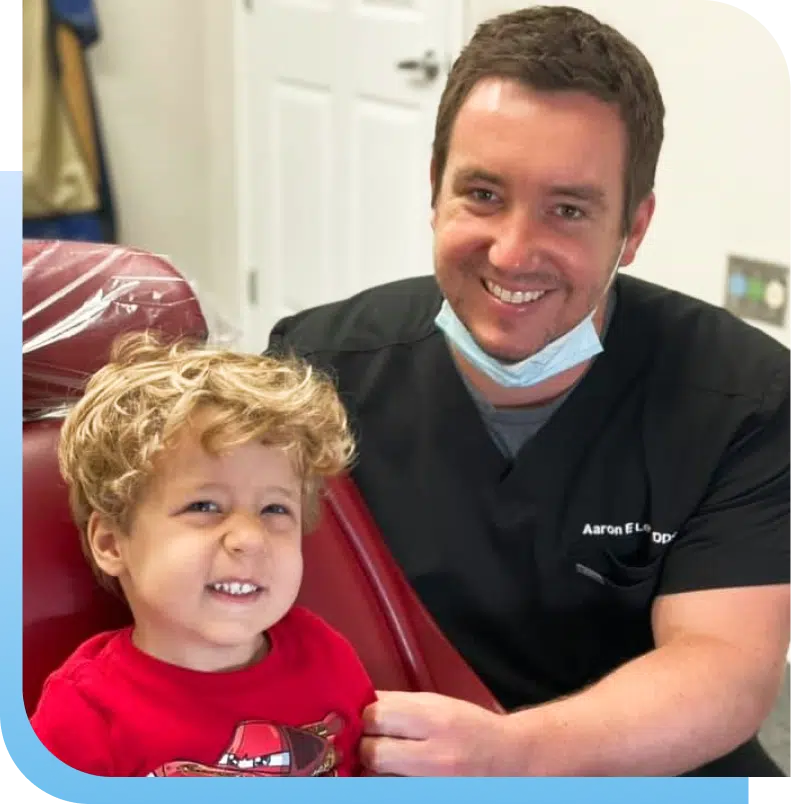 Pediatric dentist smiling with young child patient in dental office setting.