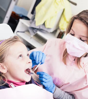 Pediatric dentist examines young girl's teeth during dental checkup in clinical setting.