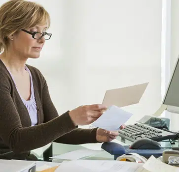 Woman in office reviewing document at desk with laptop and dental equipment visible.