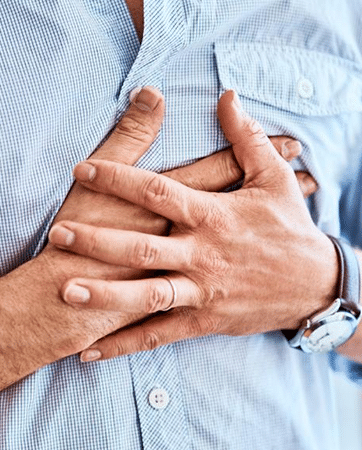 Man holding hands over stomach in light blue shirt, suggesting digestive discomfort or concern.