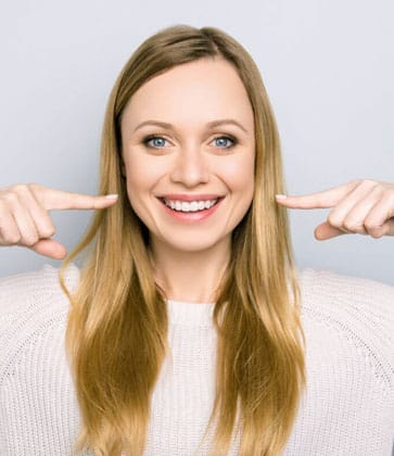 Woman smiling while pointing to her teeth in dental office setting