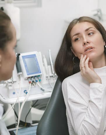 Woman patient touching face during dental consultation with hygienist in modern dental office.