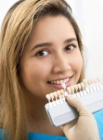Young woman smiling while holding dental shade guide samples against her teeth.