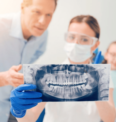 Dental professionals examining panoramic X-ray of patient's teeth in clinical setting.
