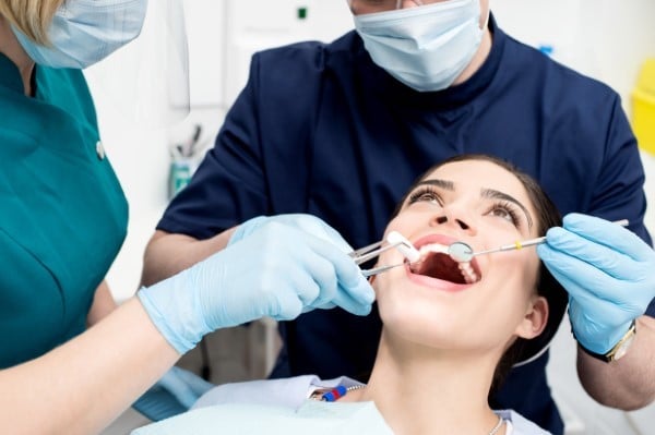 Dental professionals examining patient's teeth during routine checkup in clinical setting.