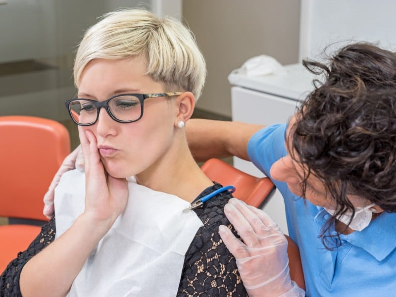 Dental professional examines young patient's mouth in clinical treatment room setting.