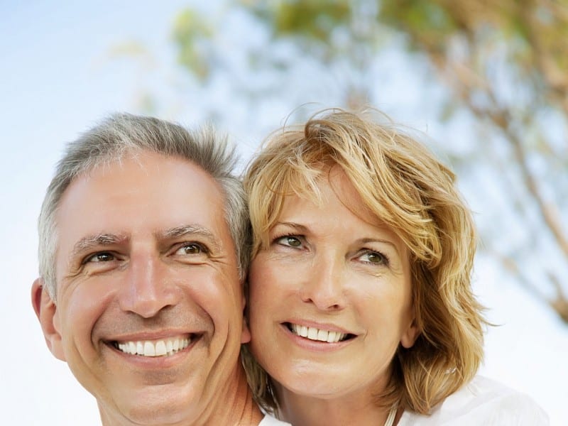 Two smiling adults posing together outdoors with blue sky and trees in background.