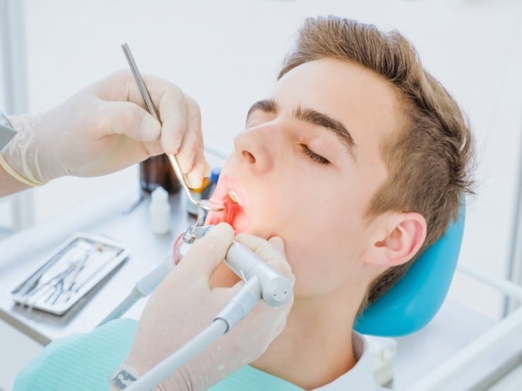 Young man receiving dental examination from dentist in clinical setting with blue chair.