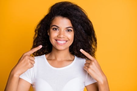 Smiling woman in white shirt against yellow background touching her hair