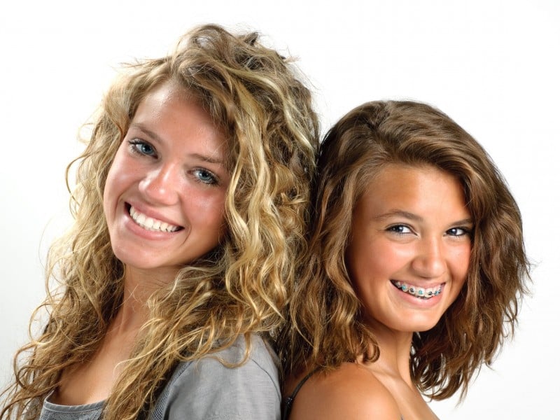 Two smiling women posing together against white background for dental practice promotional photo.
