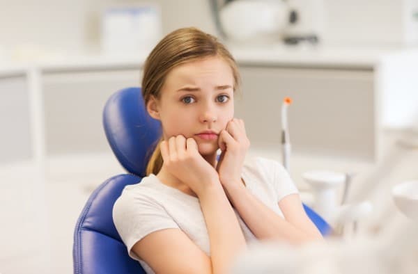 Woman in dental chair wearing white shirt, resting chin on hands, in modern dental office setting.