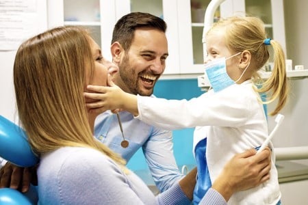 Dentist showing young child dental model while parents observe in modern dental office.