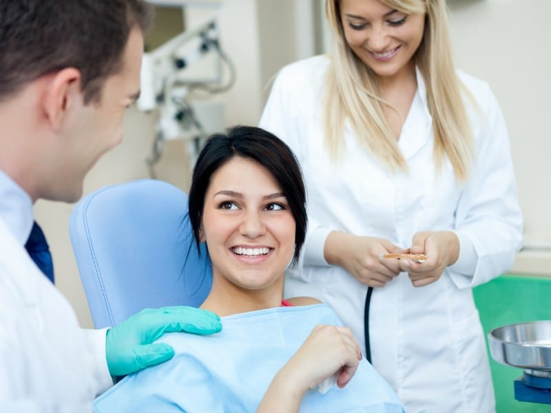 Dentist examining patient's teeth while dental assistant observes in modern clinic setting.
