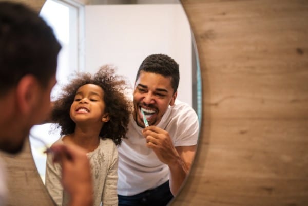 Couple brushing teeth together in bathroom mirror, smiling and practicing dental hygiene.
