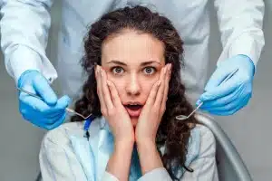 Surprised woman in dental chair with dentist's gloved hands on either side of her face.