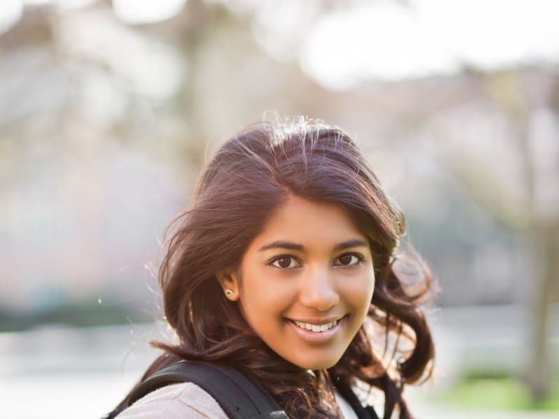 Smiling woman with dark wavy hair outdoors wearing black jacket near water
