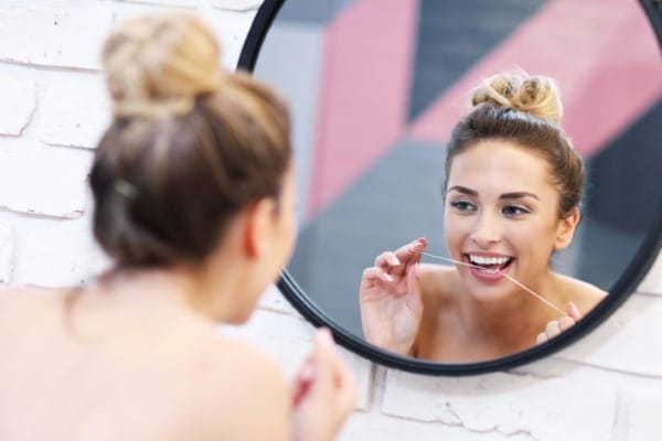 Woman brushing teeth while looking in bathroom mirror with pink and gray decor.