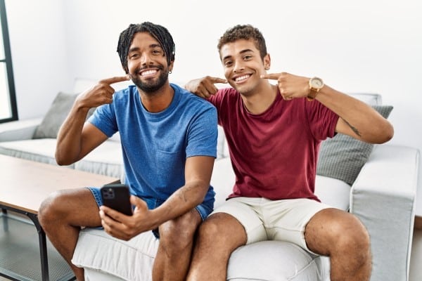 Two men sitting on couch watching sports, holding remote control and cheering enthusiastically.