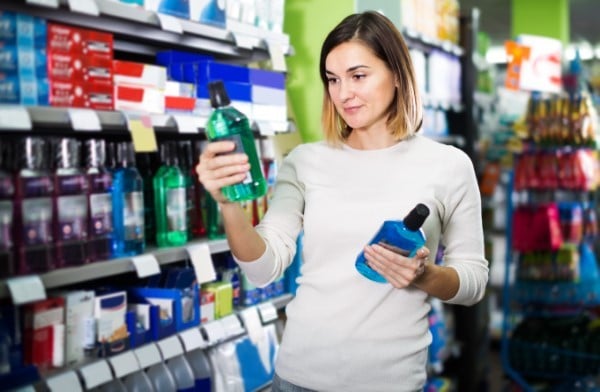 Woman comparing personal care products in store aisle, holding two bottles.