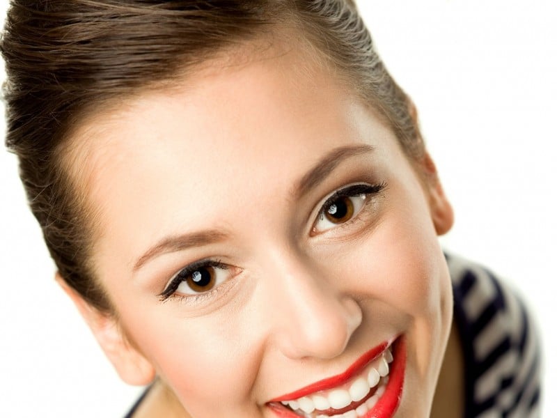 Professional headshot of smiling woman with red lipstick in dental office setting.