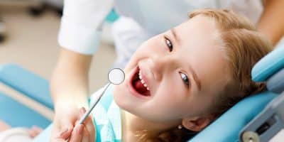 Young child receiving dental examination in dentist's chair with mirror tool visible.