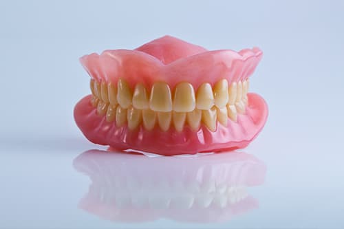 Pink full dentures displaying artificial teeth on white background for dental display.