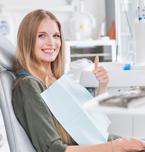 Smiling woman in dental chair giving thumbs up in modern dental office.