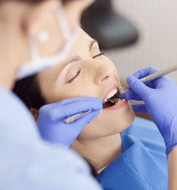 Dentist in blue gloves examining patient's teeth during dental procedure in clinical setting.