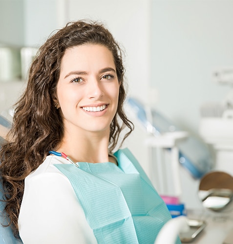 Smiling female dental professional in turquoise scrubs at modern dental office