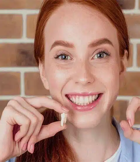 Young woman with red hair smiling while holding dental floss against brick background.