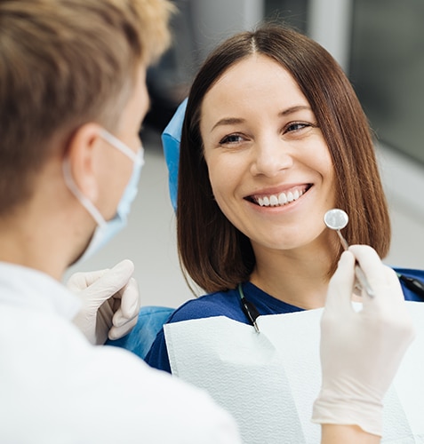 Smiling female dentist in blue scrubs examining male patient's teeth in dental office.