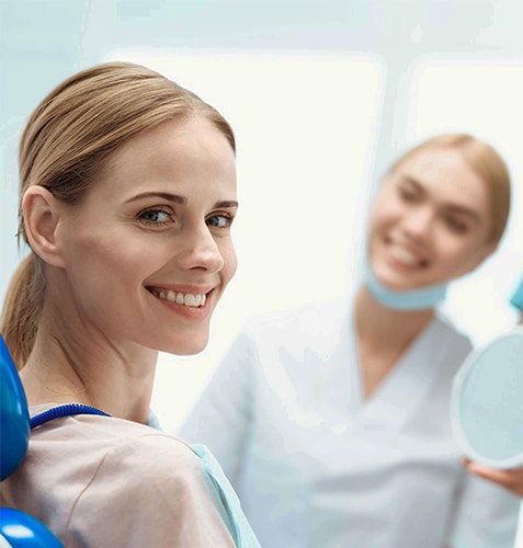 Smiling woman in dental chair with dentist and hygienist examining teeth in bright clinic.