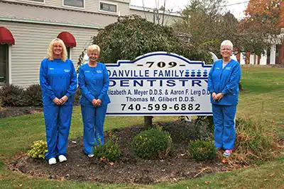Four dental staff members in blue scrubs stand behind Danville Family Dentistry sign outdoors.