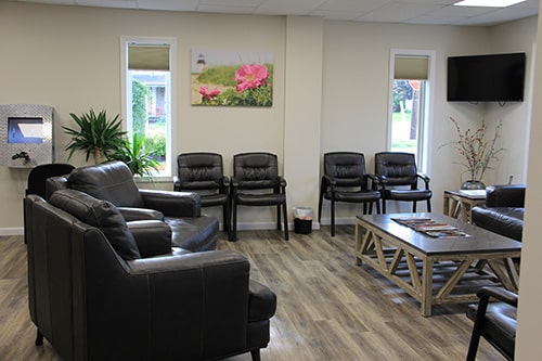 Modern dental waiting room with black leather seating, plants, and wall-mounted television.