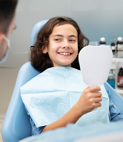 Young patient smiling in dental chair holding mirror during examination at Danville Family Dental