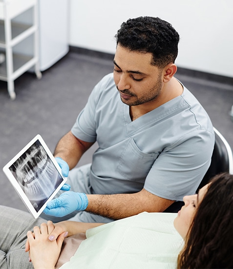 Dentist in blue gloves examining patient's teeth using digital tablet in clinical office setting.