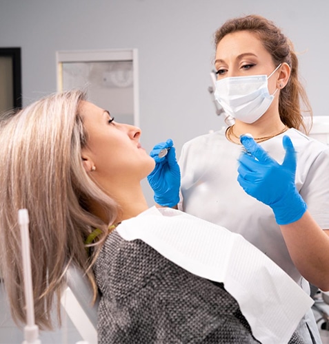 Dentist in mask and gloves examining patient's teeth in dental office
