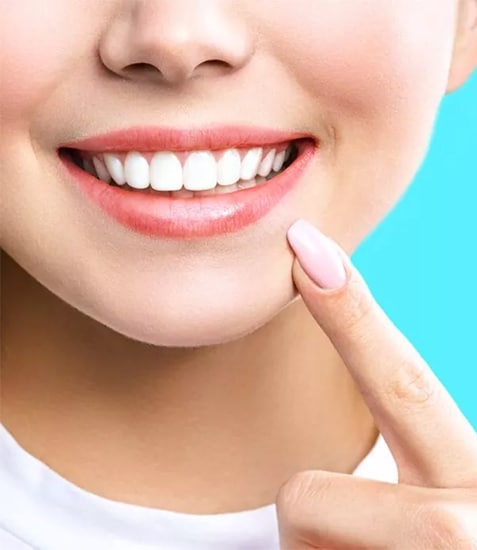 Close-up of smiling woman with bright white teeth pointing to mouth against blue background