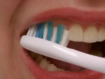 Close-up of person brushing teeth with white and blue toothbrush during oral hygiene routine.